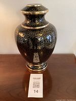 Full frontal view of the large black cloisonné urn with floral outlines and silver trim on a wooden surface.