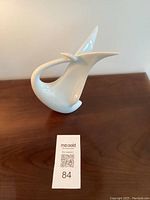 Side view of glossy white ceramic swan figurine on a wooden surface with a lot number card nearby