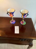 Two colorful Picasso style martini cups photographed on wooden table from a distance.