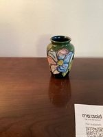 Front view of small Moorcroft vase showing floral design on an olive green background.