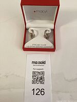 Pair of sterling silver diamond hoop earrings in Macy's branded red jewelry box with white interior and labeled display card showing metal and diamond details.