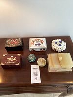 Front view of all seven trinket boxes laid out on wooden table showcasing different materials and decorative designs