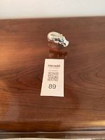 Silver plated hippo paperweight standing on a wooden surface next to a MaxSold lot ticket.