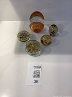 Full view of the 5 vintage glass art paperweights arranged on a white surface showing various shapes and designs.