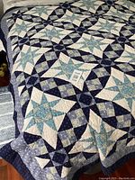 Full view of the vintage handmade quilt laid flat, showing overall pattern and color scheme of blue, navy, cream, and light green fabrics in star and ring patchwork design.