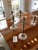 Pair of silver plated candelabras on wood table, full view