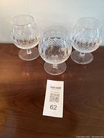Three Waterford Crystal Colleen brandy glasses on a wooden surface, showing detailed cut crystal patterns.