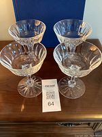Four clear crystal Waterford Innisfail champagne/tall sherbert glasses arranged on wooden surface with a blue background visible.