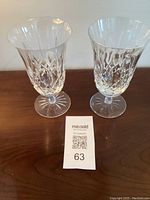 Two Waterford Lismore ice beverage glasses on a wood surface with a MaxSold lot card in front.