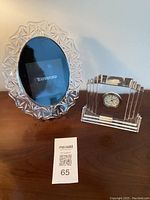 Photo showing both Waterford crystal oval picture frame and Metropolitan medium clock together on wood surface with lot tag.