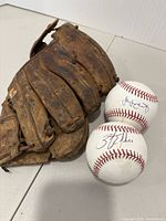 Baseball glove and two signed baseballs placed together for size and condition assessment