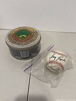 Closed vintage baseball tin next to signed baseball in plastic bag