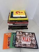 Photo of 14 stacked books about art and culture on a white surface, titles visible including Tutankhamen, Impressionism, Life: The Brand, and Eyewitness Books Arms and Armor.