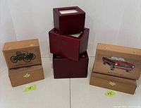 Overall view of 13 of the wooden boxes, showing 8 smaller boxes with motorcycle graphics on the left, 5 larger boxes with classic car graphics on the right, and 3 polished reddish boxes with glass tops stacked center back.