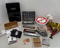 Wide shot showing the black EDGE box, harmonicas, Swiss Army tools, grooming set, pen set, patches, pipe, and other collectible items on a table.