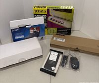 General view of the lot showing original boxed Powertap Power Control Center, Coby DVD player box, sealed phone case, and a wired mouse.