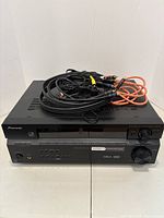 Photo showing front and top view of black Pioneer audio/video receiver with remote control and assorted cables on top.