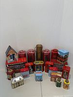 Photo showing a variety of English-themed tea tins including red phone booth tins, double-decker bus tins, a house-shaped tin, and other assorted designs.