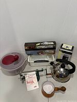 Photo of kitchen items grouped on floor including apple peeler, kettle, salad spinner, immersion blender box, tea light set, and saucepan