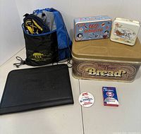 Shows a collection of tins including a bread tin, 160 marbles tin, decorative tin, a black Phillies binder, Phillies bandwagon pin, trivia game, and a blue drawstring bag.