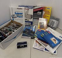Full view of varied printing supplies including paper reams, labels, computer tool kit, adhesive tapes, pens, and stapler.