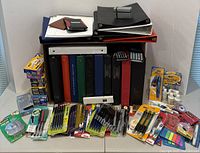 Full view of binders stacked, pens, markers, correction tapes, sticky notes, and tape dispenser laid out on table