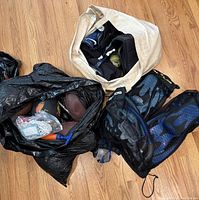 Two bags on floor containing sports and scuba gear including basketball, footballs, baseball glove, and scuba equipment.