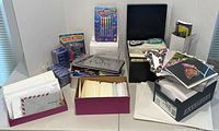 Showcases an overview of writing utensils, multiple boxes of envelopes, a purple box with cards, and a black case with other stationery supplies