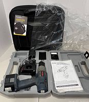 Ryobi power drill with charger and instruction manual inside gray plastic hard case alongside new Targus laptop case inside plastic wrapping