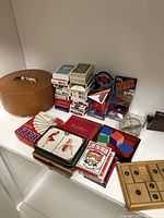 Collection of vintage playing cards, novelty cards, boxed card games, collectible toy cars in packaging, novelty poker chips, and other old school toy items on a white table.