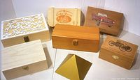 Multiple wooden boxes arranged including carved floral, printed, and painted lids plus one pyramid box