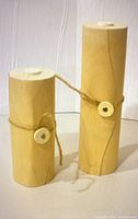 Two wooden cylindrical containers shaped like batteries, tied with twine and wooden discs, displayed closed.