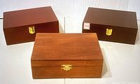 Three wooden boxes with metal clasps, smooth wood finish, shown closed with different clasp styles.