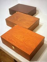 Three wooden storage boxes displayed stacked together, showing various wood tones and metal clasps on front.