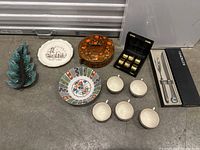 Photo of all items laid out including ceramic Christmas tree, plates, covered casserole dish, cream cups, silver plated cruet set, and boxed knives.