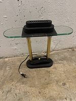 Full view of black and gold table lamp with glass shelf, showing black base, gold supports, and top section with ventilation holes.