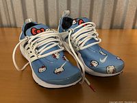 Front and side profile view of the Hello Kitty runners showing light blue fabric upper with Hello Kitty print, white soles and white laces.