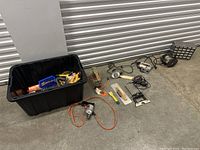 Wide view of lot including large black bin with tools and various power tools lined on the floor.