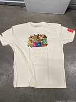 White Nintendo Switch themed T-shirt laid flat on floor showing front with group of characters