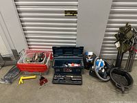 Wide shot showing the entire lot including a red plastic bin with tools, blue toolbox, portable vacuum, clamps and stands, black oil drain pan, yellow caulking gun and red clamp.