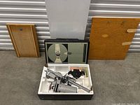 Photo of vintage photo enlarger kit with main unit, wooden plates, and case in original packaging.