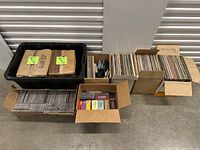 Photo of multiple boxes and bin of vinyl records and CDs arranged on concrete floor, including classical music collections and miscellaneous music media.