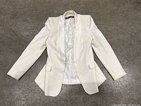 White Zara women's blazer jacket laid flat on a gray surface, showing front side with open lapels, flap pockets, and long sleeves.