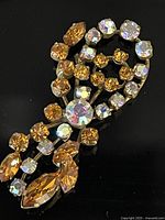 Full view of the antique pin showing amber and AB stones hand set with claws in various round and marquise shapes on a long silhouette metal backing.