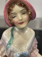 Close-up of the figurine's face showing detailed hand-painted features with pink bonnet and curly brown hair