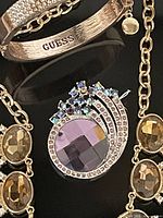 Close up of Guess engraved bangle bracelet and decorative swirl pin with purple stones