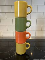 Stacked view of four coffee mugs showing their vibrant colors and D shaped handles, demonstrating stackable design.