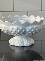 Side profile of the white milk glass bowl showing hobnail texture, scalloped rim, and pedestal base.