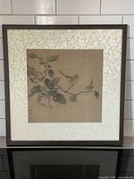 Framed square silk painting showing bird on branch with fruits and leaves, mounted with decorative textile mat and wooden frame without glass.