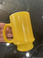 Yellow milk glass textured pedestal mug shown being held, displaying D-handle and lemon peel texture.